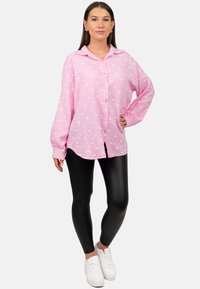 Camicia rosa con bottoni, a maniche lunghe e colletto, con fantasie a forma di cuore, abbinata a leggings neri e sneakers bianche.