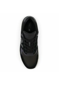 Zapatilla deportiva negra con parte superior de malla y ante, puntera reforzada, lengüeta acolchada y suela blanca. Incluye detalles reflectantes y logotipo.