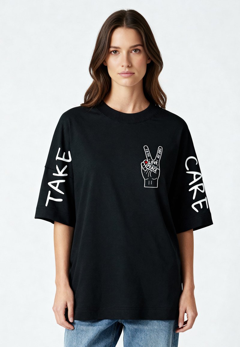 Svart bomull t-shirt med korta ärmar, med vit text "TAKE" och "CARE" på ärmarna samt en fredshand-illustration på bröstet.