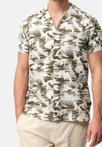 Kurzärmeliges Hemd aus strukturiertem Stoff mit einem grünen und weißen abstrakten Muster; verfügt über einen Kragen und eine durchgehende Knopfleiste.