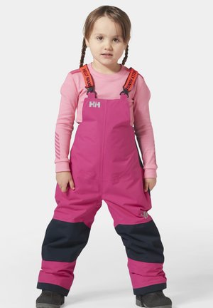 Overoles impermeables rosas con tirantes naranjas ajustables, combinados con una camiseta de manga larga rosa, usados por un niño. Presenta detalles en azul marino.