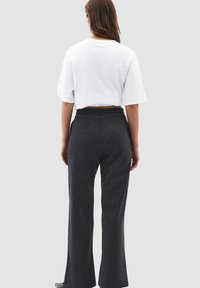 Witte T-shirt met korte mouwen en donkergrijze strepenbroeken. De broeken hebben een riemlus en een recht model.