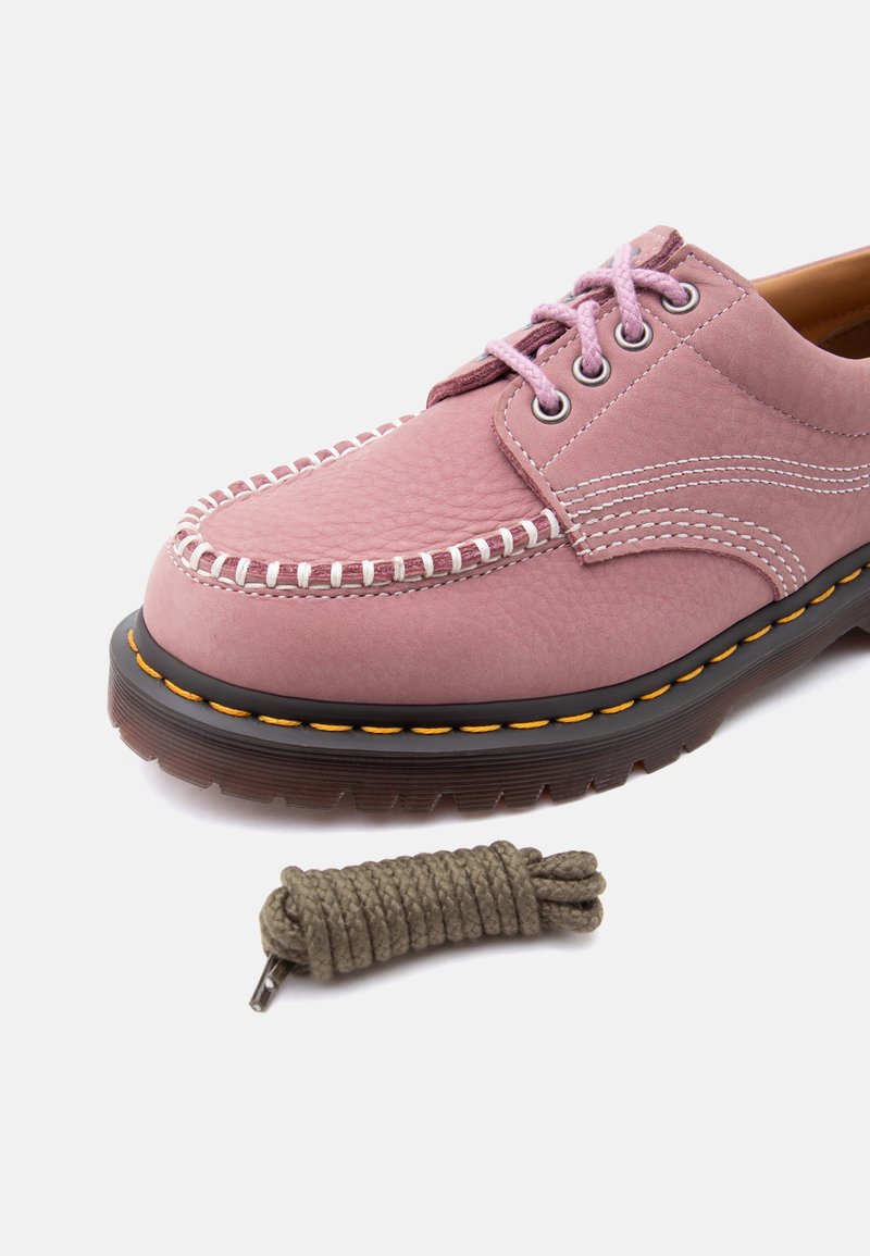 Scarpa stringata in pelle rosa con cuciture bianche, suola spessa nera con cuciture gialle e un laccio marrone avvolto separato sotto di essa.