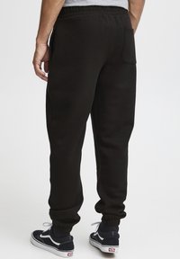 Sorte bomulds jogger bukser med elastisk talje og manchetter. Har en baglomme og sidelommer, parret med marineblå sneakers.