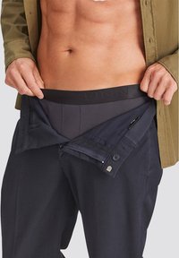 Black trousers with a zippered fly, revealing gray boxer briefs with "FINN" branding. Shirt is olive green, slightly unbuttoned.