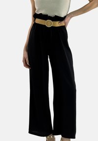 Schwarze Hose mit weitem Bein aus leichtem Stoff, elastischem Bund und kontrastierendem, braunem Gürtel mit runder Metallschnalle.