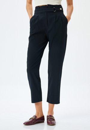 Black tailored trousers with pleats, belt loops, and a side button detail. Cropped length with pockets; sleek fabric texture.
