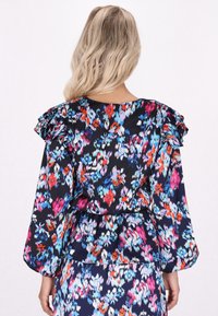 Blůza s dlouhým rukávem s tmavým květinovým vzorem, která má volány na ramenou a peplum pas, vyrobená z lehkého materiálu.