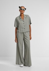 Striped green two-piece outfit featuring a cropped button-up shirt with short sleeves and wide-leg trousers, paired with white shoes.