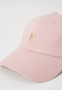 Cappellino da baseball rosa realizzato in tessuto testurizzato, con un accento del logo dorato sulla parte anteriore. La visiera è curva e il design è semplice.