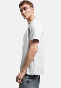 Kortærmet, lysegrå t-shirt i blødt stof med rund halsudskæring og en afslappet pasform, parret med slidte blå jeans.