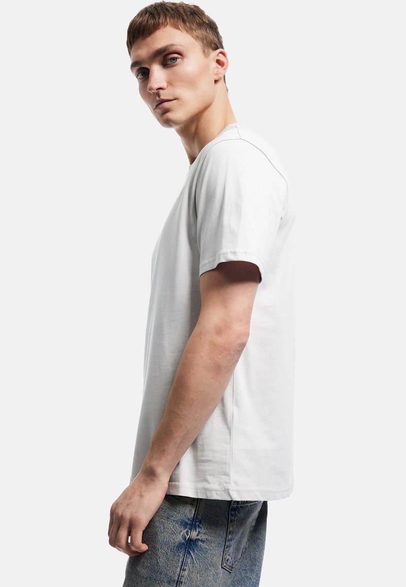 Kortærmet, lysegrå t-shirt i blødt stof med rund halsudskæring og en afslappet pasform, parret med slidte blå jeans.