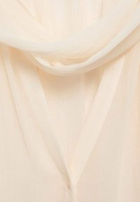 Tissu léger beige clair transparent avec une texture douce et fluide, délicatement drapé et superposé pour créer un effet délicat et translucide.
