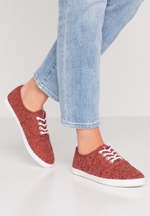 Czerwone sneakersy z koronką, z białymi gumowymi podeszwami, okrągłym przodem i białymi sznurówkami. Posiadają teksturowany wzór koronki dla dodatkowego zainteresowania wizualnego.