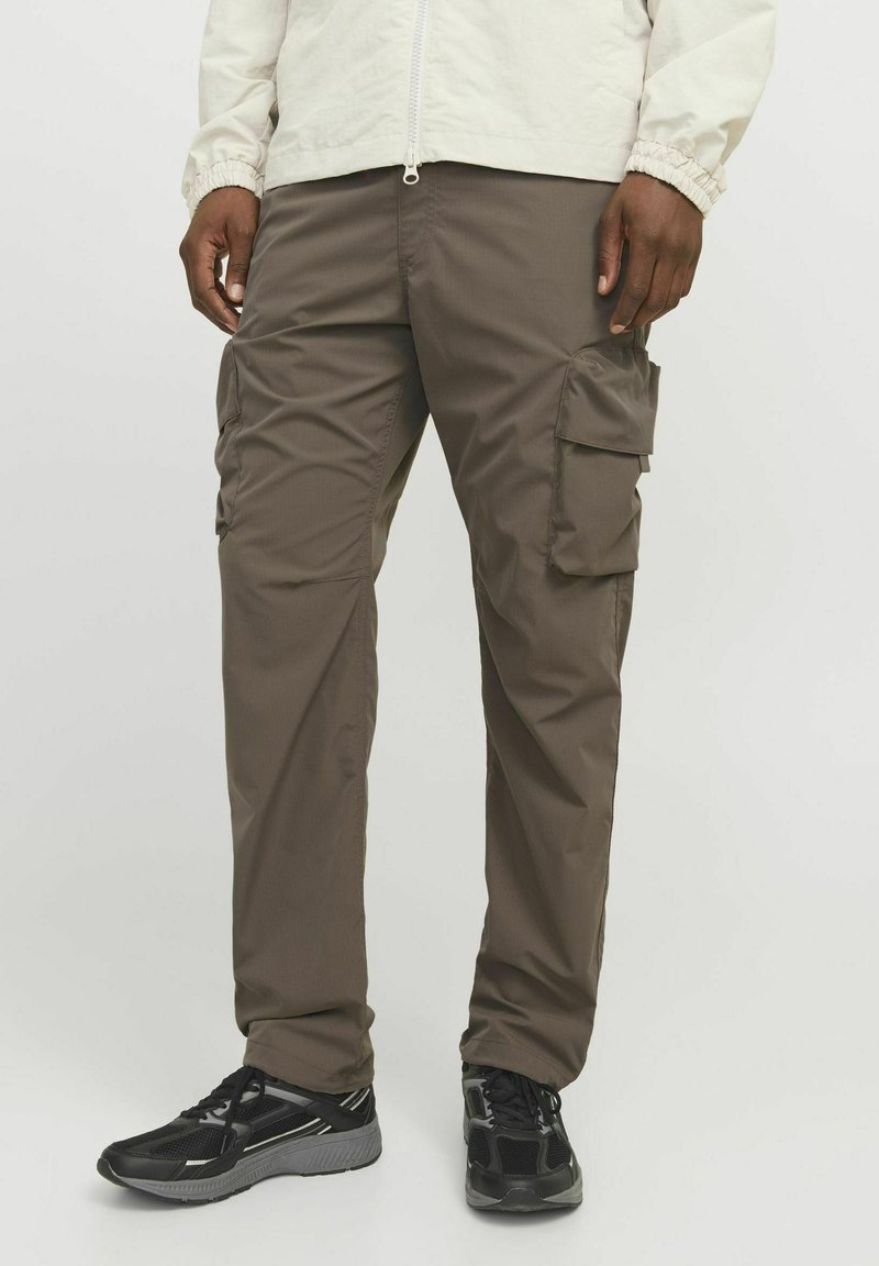 Pantalones cargo marrones confeccionados en tejido ligero, con múltiples bolsillos laterales y un corte relajado, combinados con zapatillas deportivas negras.