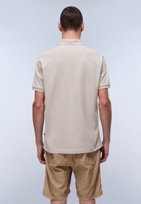 Beige polo shirt med korte ærmer og regular fit, der har en klassisk krave og tekstureret stof. Sammen med brune shorts.