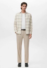 Beige karierter Hemd mit Knöpfen, kombiniert mit cremefarbenen Hosen. Glatte Textur, lockere Passform und akzentuiert mit einem schwarzen Gürtel und Schuhen.