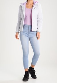 Giacca trapuntata grigia chiaro con fodera rosa, indossata sopra un top lavanda e jeans skinny blu. Sneakers nere completano il look.
