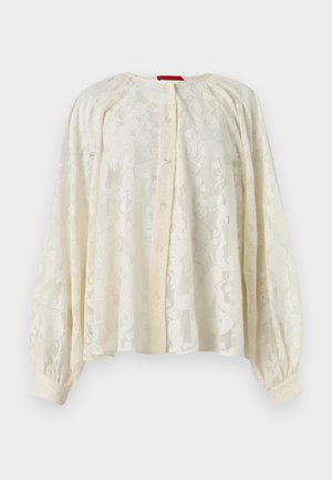 Kermanvärinen pitsinen pitkähihainen paita, jossa napitettava etuosa, kerätty pääntie ja kalvosinvarret, valkoisella taustalla.