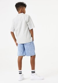 Gestreept kortemouwshirt in wit en grijs, gecombineerd met blauwe denimshorts. Witte sneakers met zwart-witte gestreepte sokken zichtbaar.