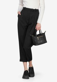 Pantaloni neri plissettati abbinati a un maglione aderente bianco a costine, sneakers nere e una piccola borsa a tracolla in pelle nera con dettagli dorati.