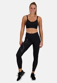 Czarny sportowy top typu crop oraz legginsy z wysokim stanem w subtelny wzór diamentów. Materiał wydaje się elastyczny; zestawione z czarnymi butami sportowymi.