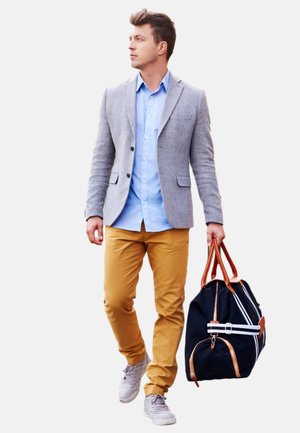 Grauer Blazer über einem hellblauen Hemd, beigen Hosen und grauen Sneakers. Trägt eine marineblaue Reisetasche mit braunen Ledergriffen und weißen Akzenten.