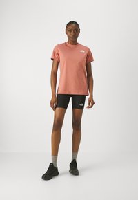 Roosa puuvillane T-särk ümmarguse kaelusega ja The North Face logo vasakul rinnal, koos mustade jalgrattashortside ja mustade spordijalatsitega.