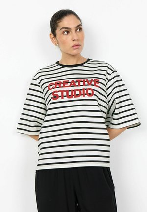 Woman in black and white striped shirt with "CREATIVE STUDIO" in red text, looking slightly to her left against a white background.