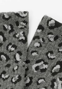 Šedá pletená látka s leopardím vzorem v černé a světle šedé barvě, ukazující různorodé skvrny po celé ploše s jemnou strukturou.