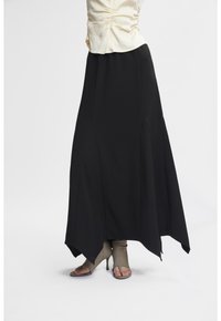 Gonna maxi nera con orlo asimmetrico, realizzata in un materiale fluido, con cuciture laterali e una texture liscia. Indossata con un top leggero.