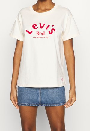 Crèmekleurig T-shirt met korte mouwen met rode "Levi's Red" grafische tekst, ronde halslijn en een ontspannen pasvorm, gecombineerd met een denim minirok.