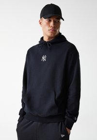 Sudadera con capucha negra, con un bolsillo frontal, material de algodón ligero, cordones ajustables y un pequeño logo blanco en el pecho.