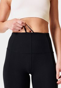Leggings neri a vita alta con una texture liscia e cuciture strutturate. Bretelle regolabili in vita per una vestibilità personalizzabile.