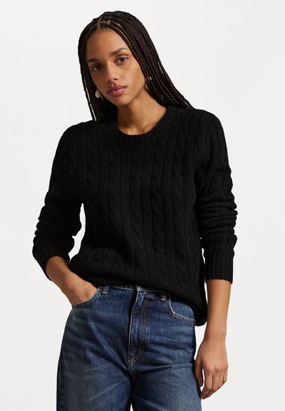 Μαύρο πουλόβερ με πλέξη καλωδίου και στρογγυλή λαιμόκοψη, με μακριά μανίκια και ριμπ μανσέτες, σε συνδυασμό με μπλε τζιν παντελόνι. Είναι ορατή η υφή του υφάσματος.