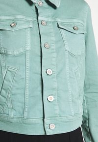 Giacca di jeans verde menta con collo, due tasche sul petto e chiusure a bottone argentato. Presenta un design cropped e un tessuto texture.