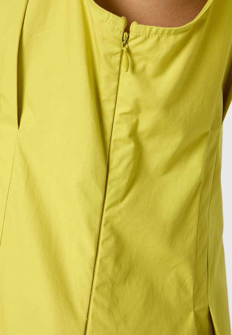 Limegrön topp med rundad halsringning och en centralt placerad dragkedjedetalj, med en mjuk tygtextur och rena, enkla designlinjer.