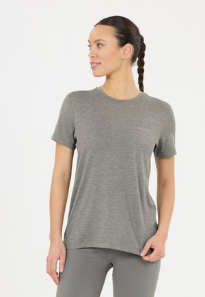 Vrouw met gevlochten haar die een grijs sportshirt met korte mouwen en bijpassende legging draagt, kijkt naar links tegen een effen achtergrond.