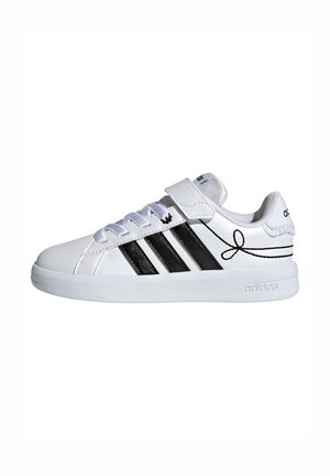 Baskets blanches Adidas avec des bandes noires, strap à scratch, lacets blancs et surpiqûres décoratives noires sur le côté.