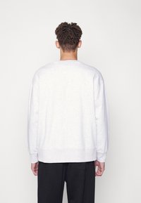Sudadera gris con un corte relajado, puños y bajo acanalados, y una textura suave, combinada con pantalones negros, vista desde la parte posterior.