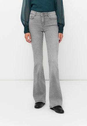 Jeans grigi flared con vita alta, dotati di tasche anteriori e una texture liscia. Abbinati a un top lungo a maniche trasparenti di colore teal.
