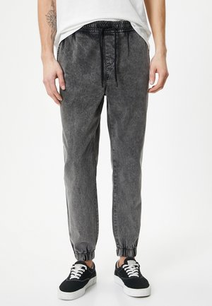 Grijze joggerbroeken van denim, met een elastische tailleband en trekkoord, taps toelopende pijpen en geribde boorden. Gedragen met zwarte sneakers.