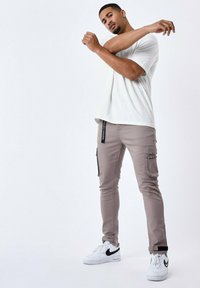 Pantalones cargo beige con bolsillos laterales, diseño ajustado, combinados con una camiseta blanca sencilla y zapatillas blancas con acentos negros.