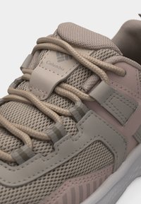 Κοντινό πλάνο μπεζ και ανοιχτό ροζ αθλητικού παπουτσιού Columbia με υφασμάτινο δίχτυ, επενδυμένη γλώσσα και στρογγυλά κορδόνια που περνούν μέσα από υφασμάτινες θηλιές.