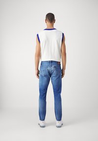 Sleeveless white top with blue trim, paired with blue denim jeans. The jeans have a fitted style and a slightly faded texture. White sneakers.