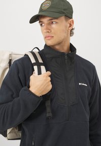 Marine fleece pullover med sort panel, lynlås krave og Columbia logo. Beiges rygsæk med et gittermønster og justerbare sorte stropper.