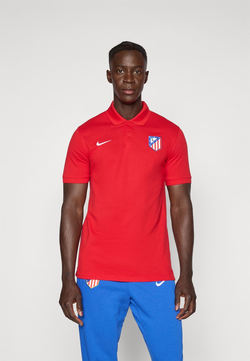 Rode polo met kraag, korte mouwen, met een Nike-logo en het embleem van Atlético Madrid. Draagt het met blauwe joggingbroek.