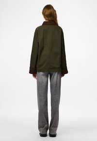 Olive roheline jakk pruuni kraega, mugav lõige ja pikad varrukad. Kombineeritud laia säärega hallide pükstega ja mustade jalatsitega.