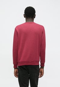 Felpa rossa in pile con maniche lunghe e polsini a costine, dotata di scollo rotondo e finitura in tessuto solido. Viene mostrata la vista posteriore.