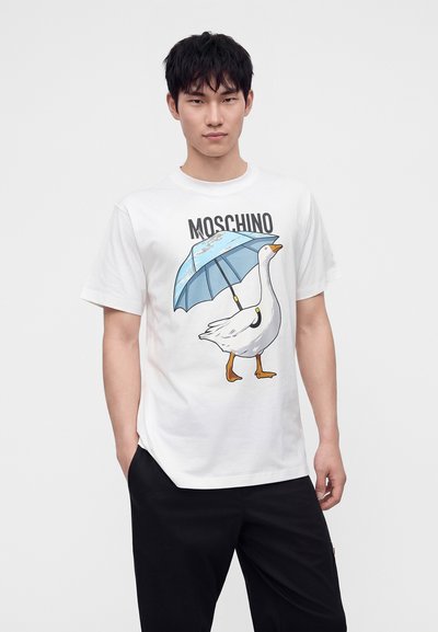 Άνδρας που φοράει λευκό T-shirt με γραφικό μιας χήνας που κρατάει μια μπλε ομπρέλα και τη λέξη Moschino από πάνω.